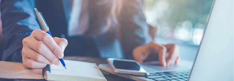 Businesswoman writing in a notebook with a pen, focused on her work in a professional setting.