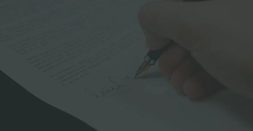 A hand signing a document with a pen, capturing the act of formalizing an agreement.