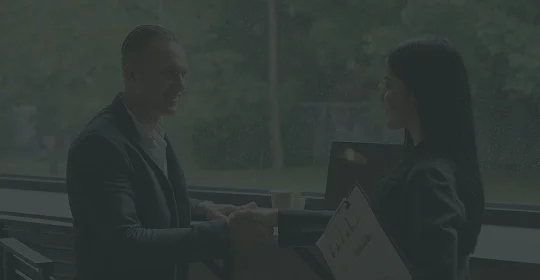A man and woman shaking hands in front of a large window, symbolizing a professional agreement or partnership.