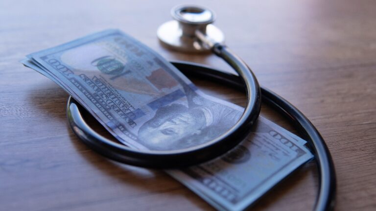 black stethoscope wrapped around a stack of U.S. dollar bills