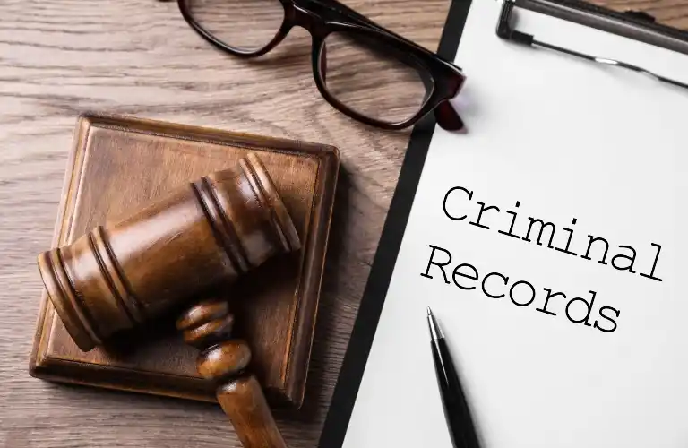 Wooden judge's gavel, eyeglasses, and clipboard with "Criminal Records" text on wooden surface.