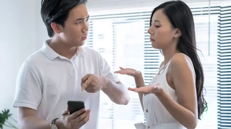 Two young adults in white clothing engaged in a serious conversation indoors.