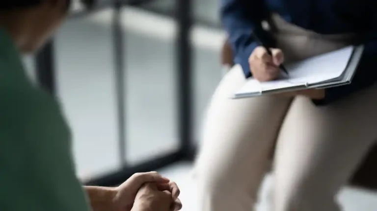 Two people engaged in a discussion, one writing on a clipboard, muted indoor setting.