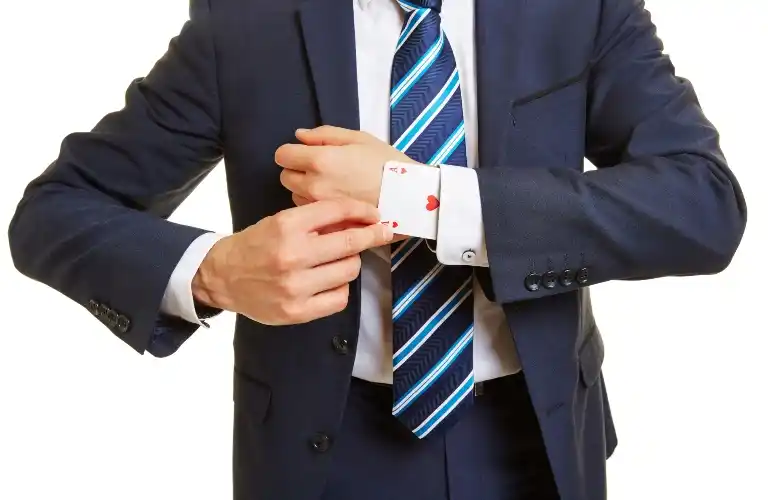Man in a navy suit revealing an Ace of Hearts playing card hidden in his shirt cuff.