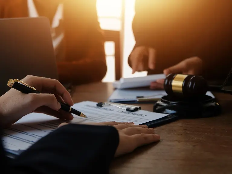 Hands signing a legal document on a clipboard beside a judge's gavel on wooden table.