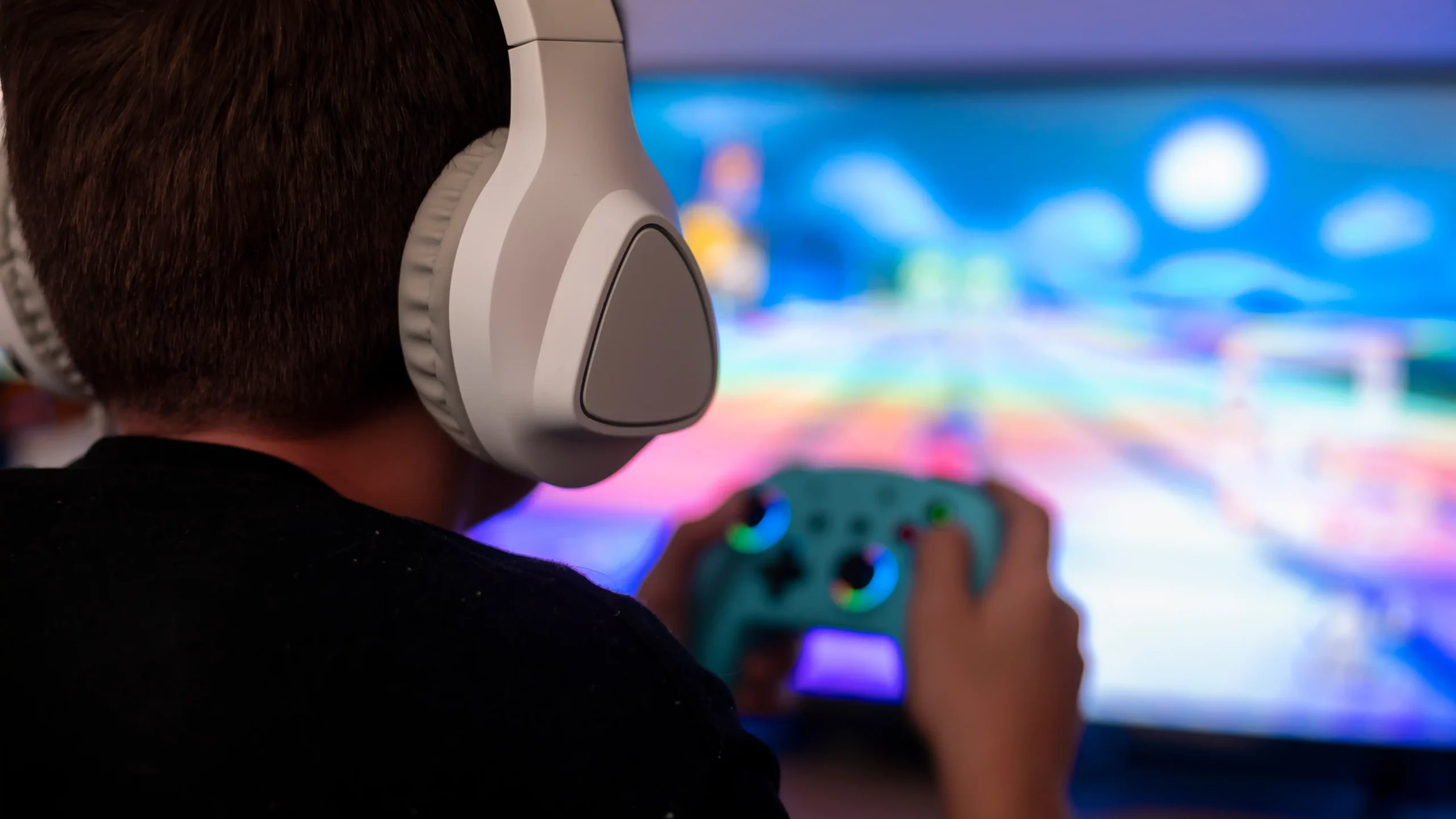 Person wearing white headphones playing a colorful video game with a blue controller.