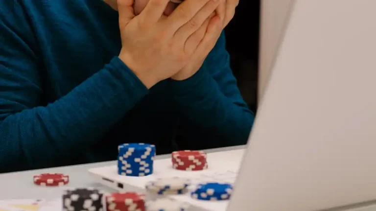 Person in blue long-sleeve shirt covering their face near poker chips and a laptop.