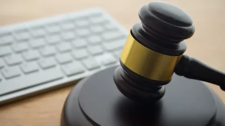 Close-up of a black judge's gavel with a gold band placed near a white computer keyboard on a wooden surface.