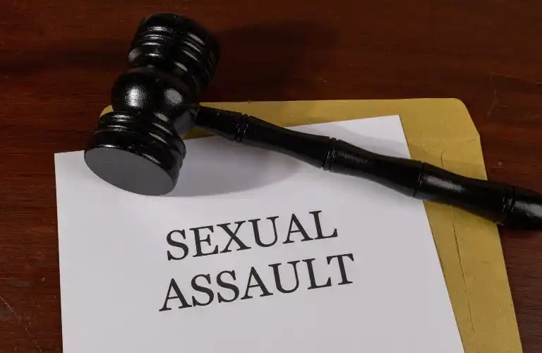 Wooden judge's gavel resting on a document labeled "Sexual Assault" on a wooden surface.