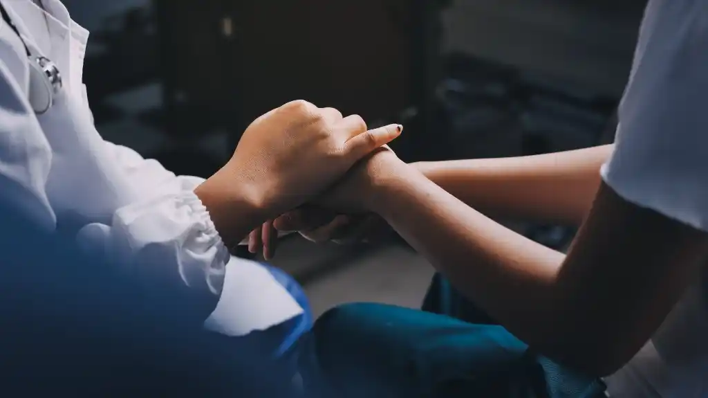 Two people holding hands in a comforting gesture, one wearing a white medical coat.
